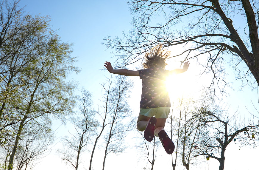 Girl Jumping Silhouette Against Sun and Trees