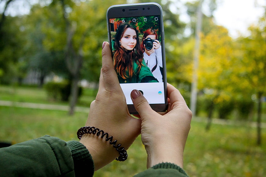 Hands holding smartphone taking photo in autumn park