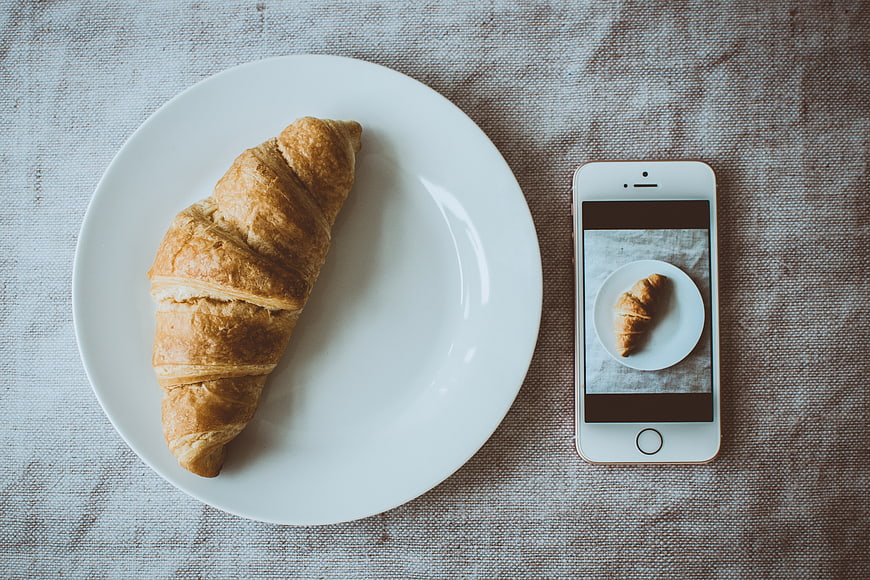 Flat lay of croissant on plate with smartphone photo