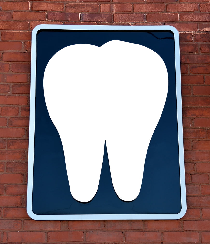 White Tooth Icon On Blue Sign Against Red Brick Wall