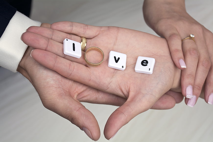 Wedding rings and Scrabble tiles spelling love in hands