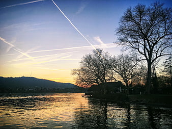 Serene Lake Sunset with Contrails and Silhouetted Trees