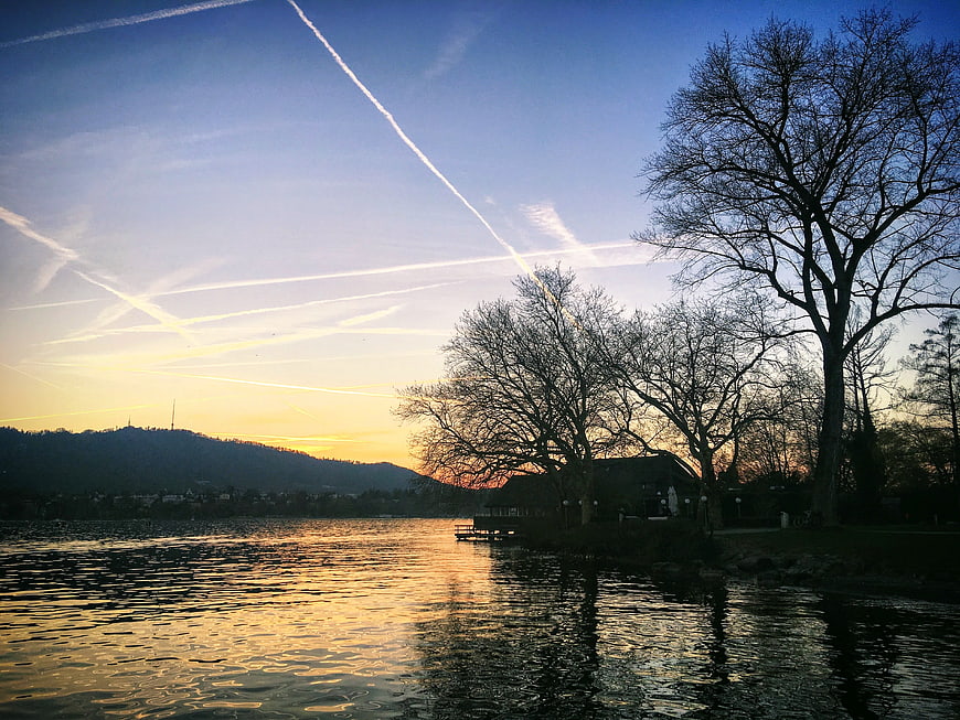 Serene Lake Sunset with Contrails and Silhouetted Trees