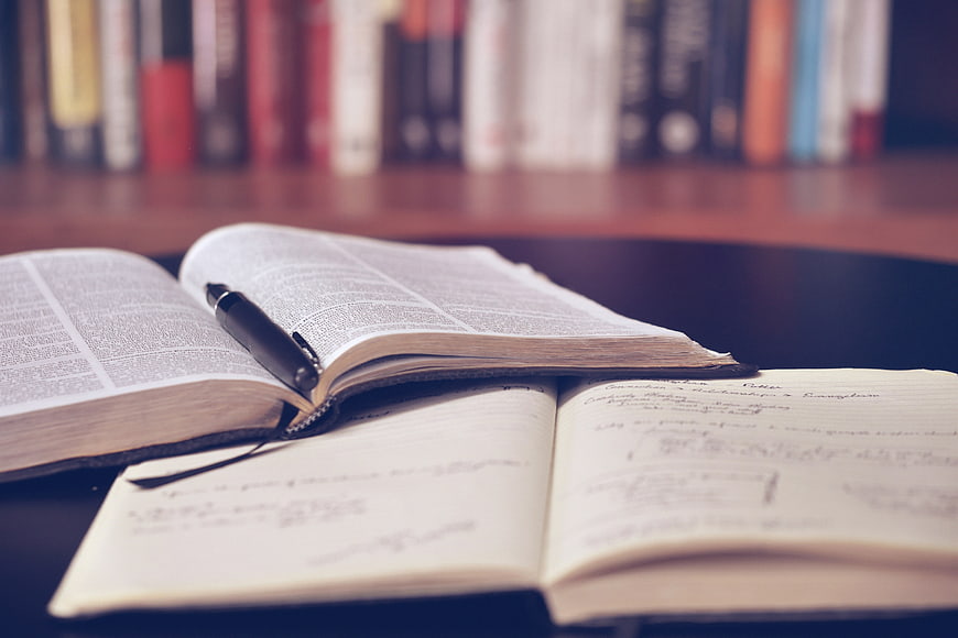 Open Bible and Notebook with Pen on Desk