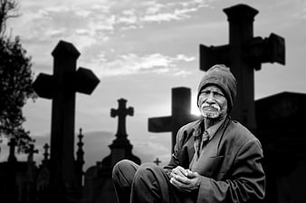 Elderly man sitting in cemetery with crosses background