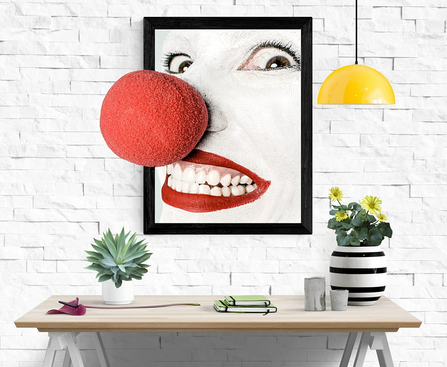 Modern office desk with surreal clown art print and yellow lamp
