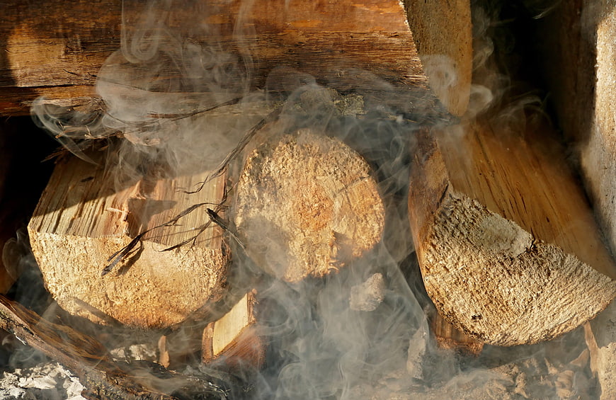 Smoldering firewood logs with rising smoke in a rustic stove