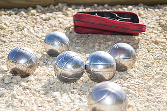 Metal bocce balls on gravel with red carrying case