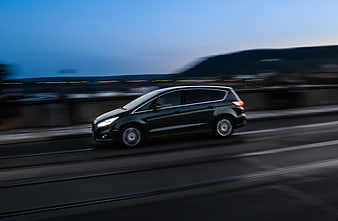 Black minivan driving fast on highway at dusk
