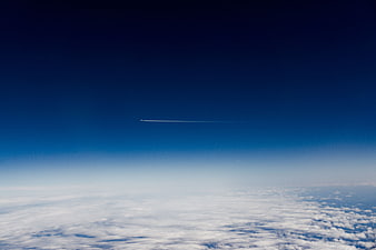 Aerial View of Contrail in Deep Blue Sky Above Clouds