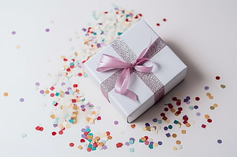White gift box with pink ribbon and colorful confetti