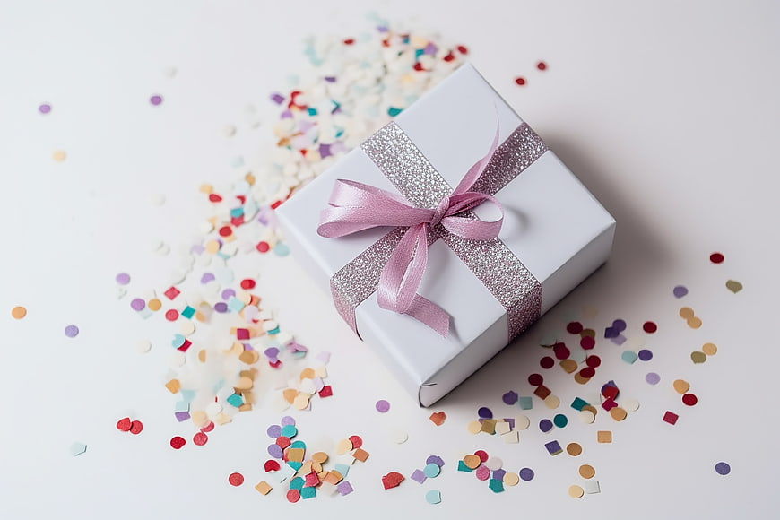 White gift box with pink ribbon and colorful confetti