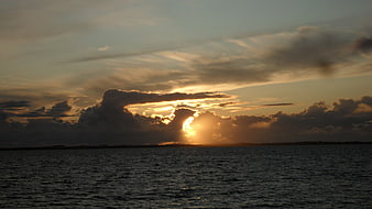 Dramatic sunset over ocean with sun breaking through clouds