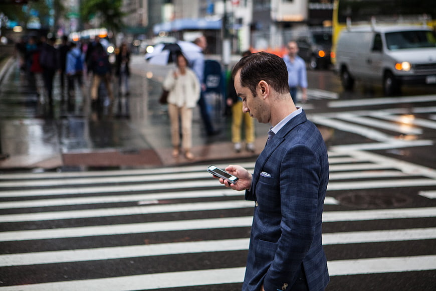 Businessman in Blue Suit Checking Smartphone on City Crosswalk