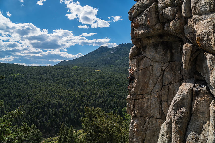 Rock climber scaling cliff face with mountain forest view