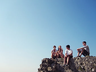 Group of friends sitting on a rocky cliff edge against a blue sky