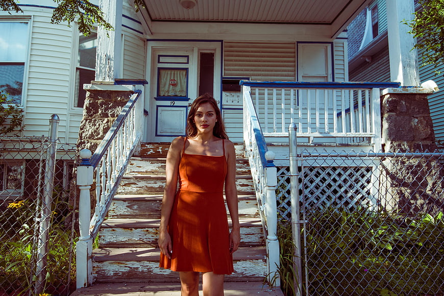 Young woman in orange dress standing on suburban porch