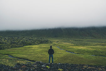 Man standing on rocky hill overlooking misty green valley
