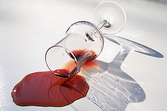 Spilled Red Wine in Tipped Glass on White Surface