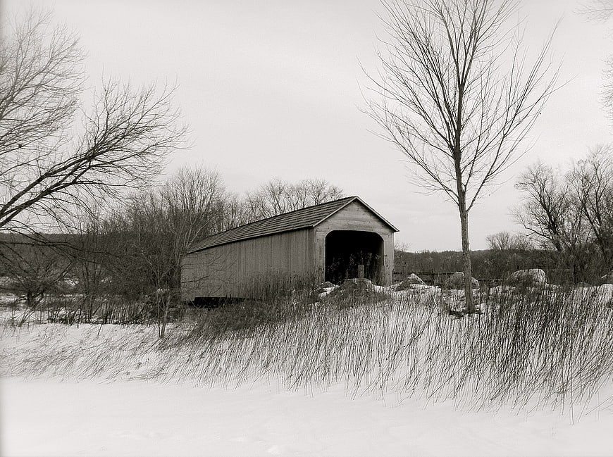 Black and white winter landscape with a rustic covered bridge