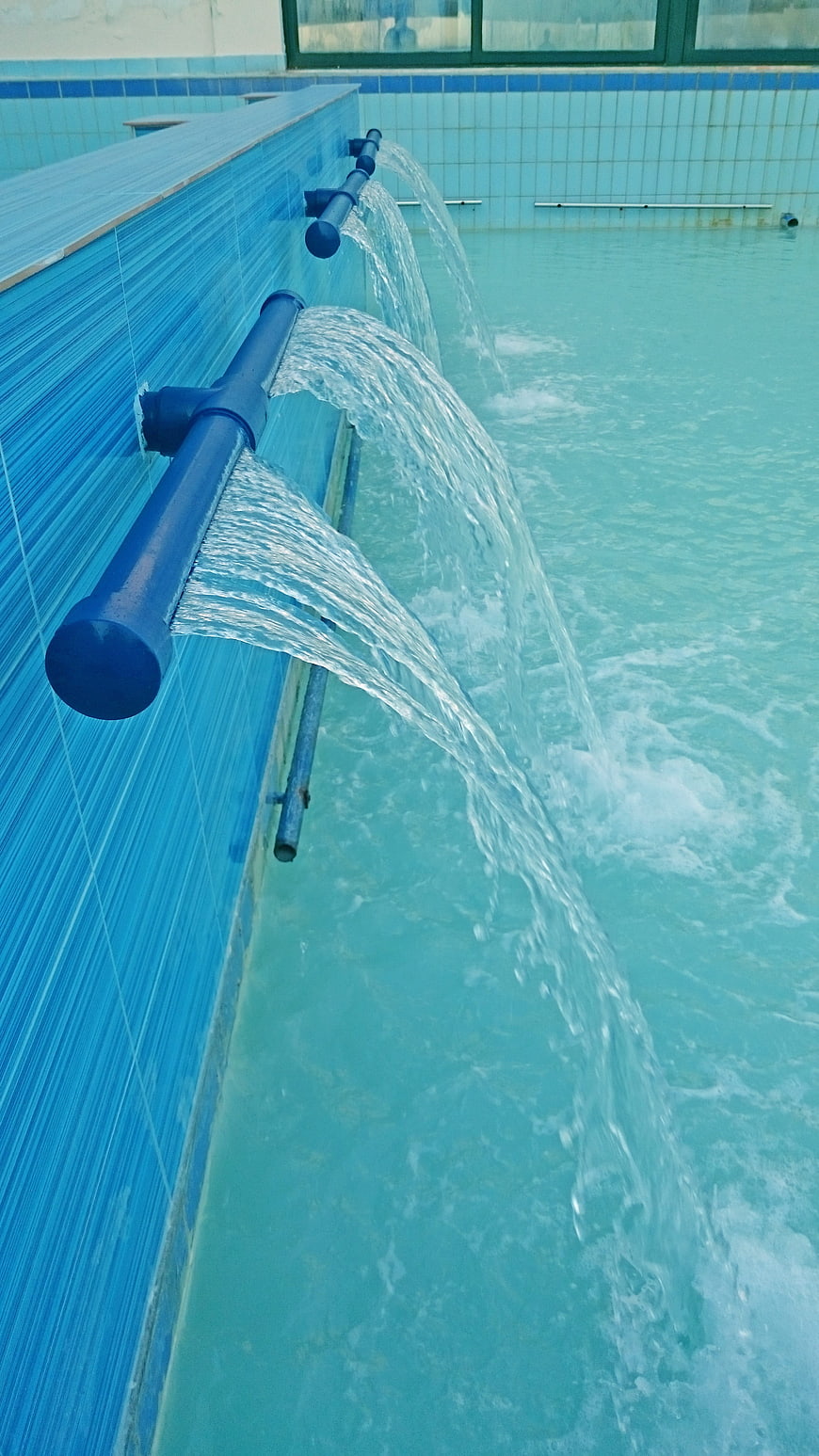 Water flowing from blue pipes into a swimming pool