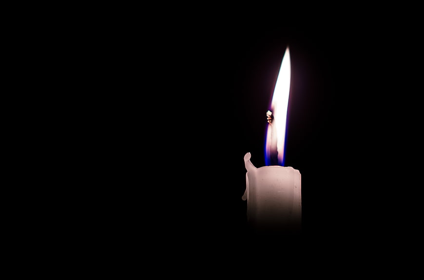 Single lit white candle flame on black background
