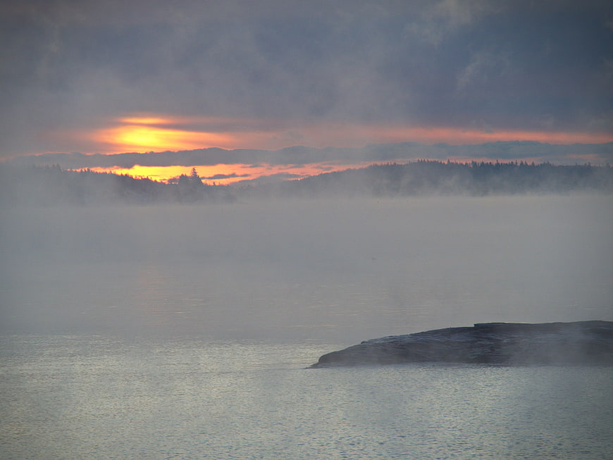Misty Sunrise Over Lake With Distant Forest Horizon