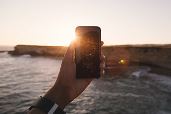 Hand holding smartphone with compass app at sunset