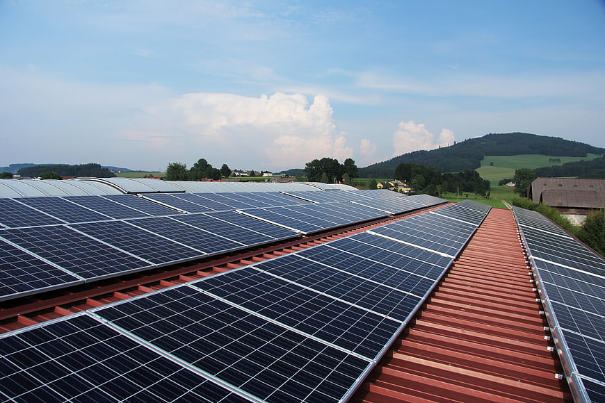 Solar panels on red roof with green hills and blue sky