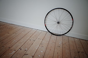 Bicycle wheel leaning against white wall on wooden floor