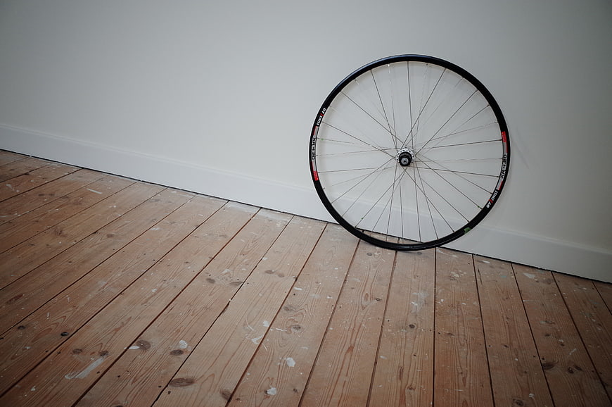 Bicycle wheel leaning against white wall on wooden floor