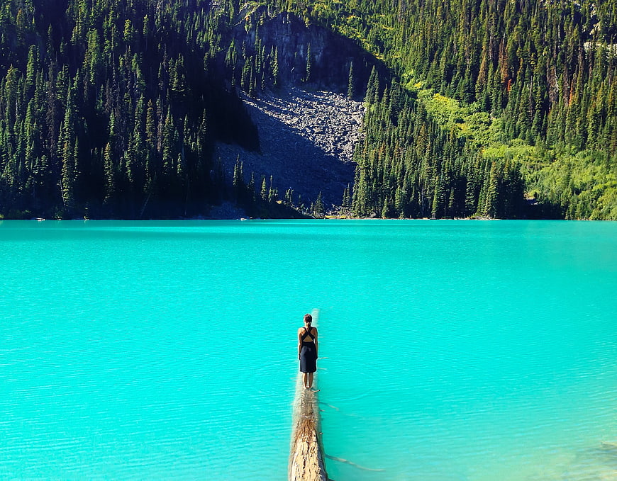 Woman standing on log in turquoise alpine lake