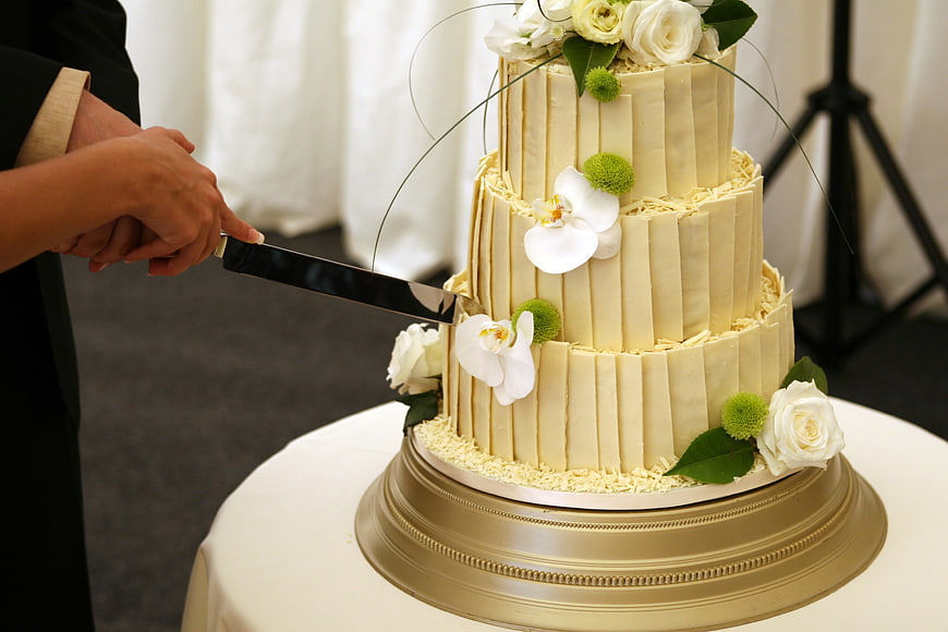 Elegant Three-Tier Wedding Cake Being Cut With Fresh Floral Decorations