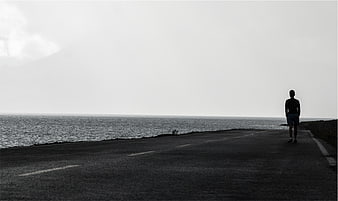 Silhouette of Man Standing on Coastal Road in Black and White