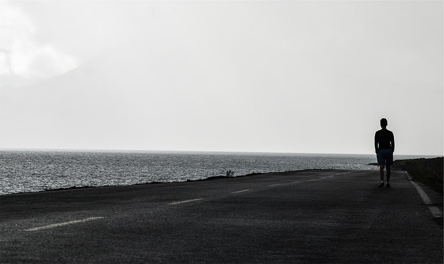 Silhouette of Man Standing on Coastal Road in Black and White