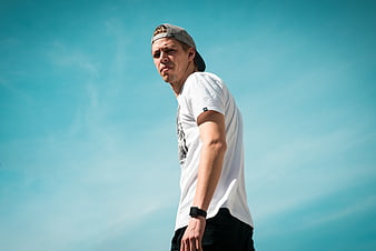Young man in white t-shirt and cap against blue sky