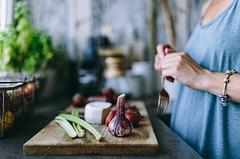 Woman preparing healthy salad with fresh vegetables on wooden board