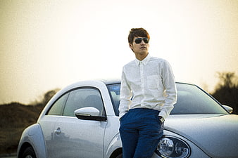 Man in white shirt and sunglasses leaning on white car at sunset