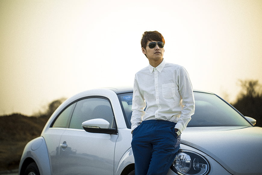 Man in white shirt and sunglasses leaning on white car at sunset