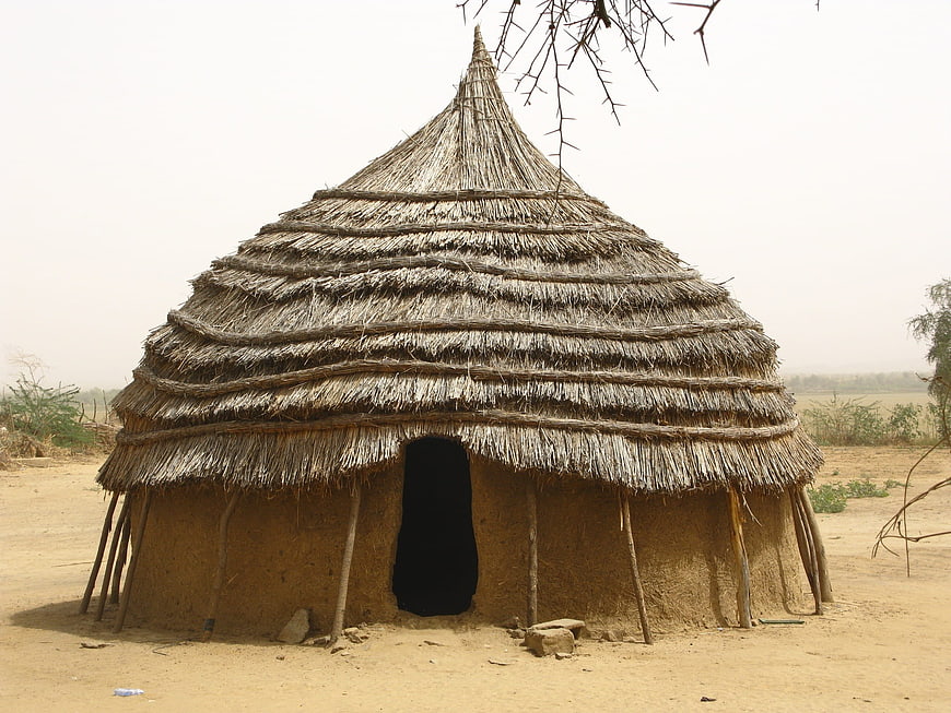 Traditional Thatched Mud Hut In Rural African Village Landscape