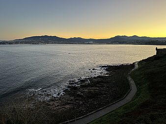Serene coastal path at sunset with distant mountains and calm sea