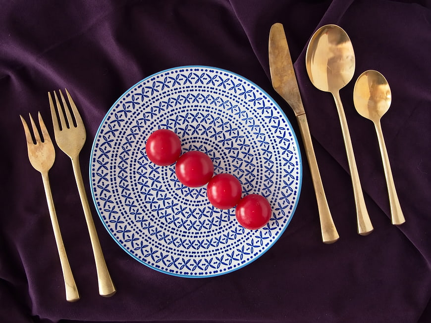 Flat lay of blue patterned plate with tomatoes and gold cutlery