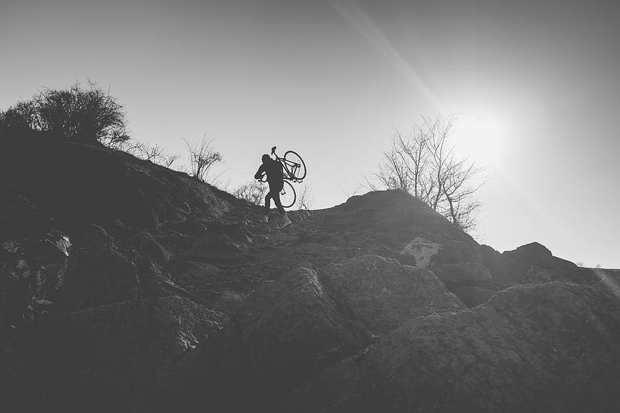 Silhouette of Cyclist Carrying Bike on Rocky Hill