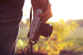 Hand holding silver mirrorless camera in golden sunlight