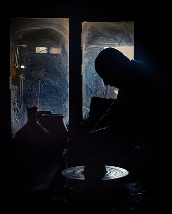 Silhouette of a potter working at a wheel in a dark workshop