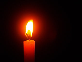 Single lit candle flame glowing against a dark black background