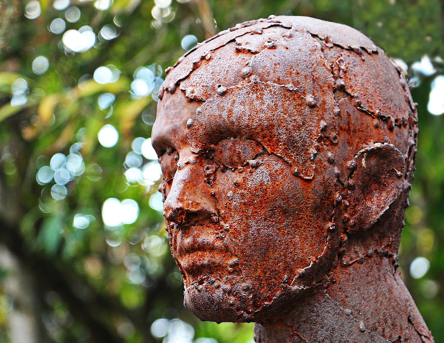 Rusty metal sculpture of a human head in profile