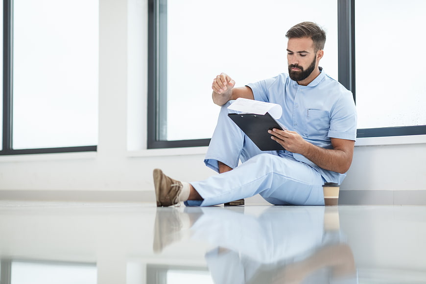 Male nurse sitting on hospital floor reading clipboard