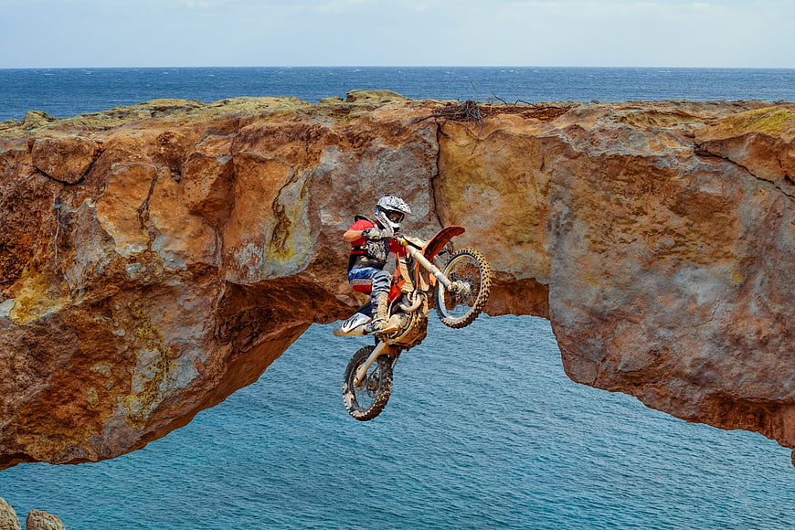 Motocross Rider Jumping Over Coastal Rock Arch