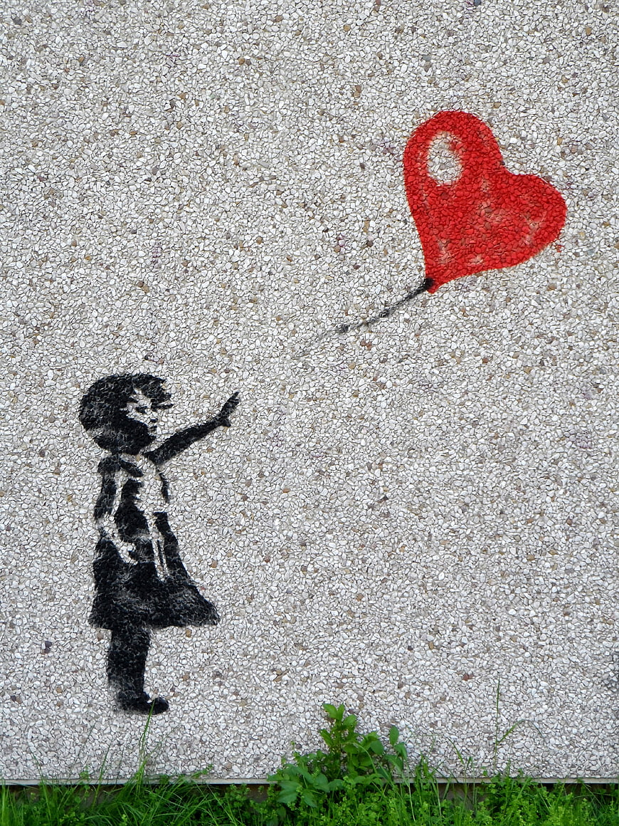 Street art mural of girl reaching for red heart balloon